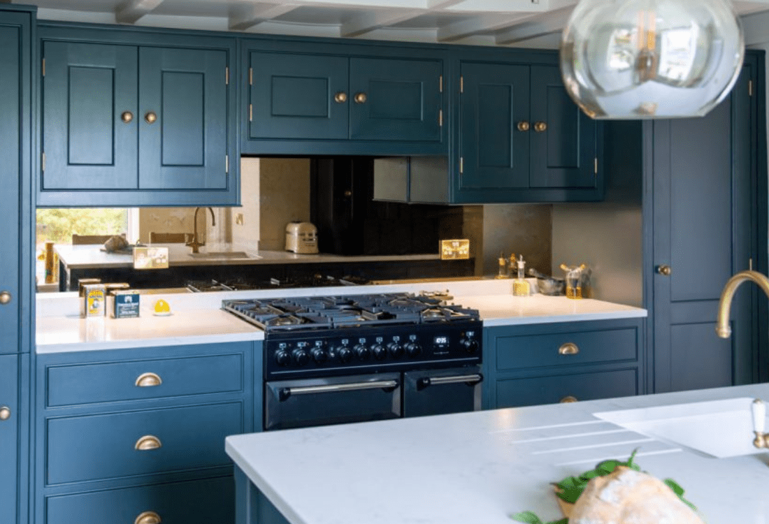 Personalised kitchen design showcasing bespoke cabinetry with dark teal units and brass hardware, a central island with a white countertop, and a large range cooker, illustrating how custom features can reflect individual style.  