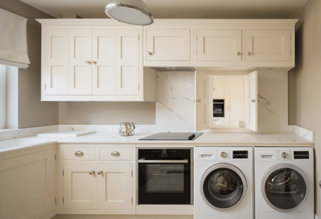 A sleek black oven and modern washing machines integrated into a classic white kitchen with shaker-style cabinets, demonstrating how modern appliances can blend into bespoke traditional kitchens.