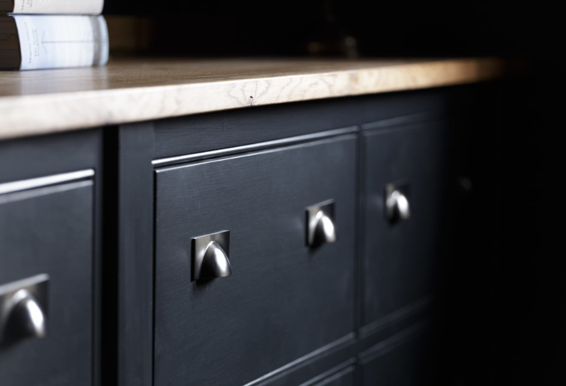 A close-up of a high-end dark kitchen cabinet with silver handles, highlighting the attention to detail and craftsmanship involved in our design process as kitchen designers. 